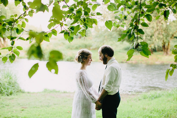 Bride and groom standing near a river holding hands by Samm Blake